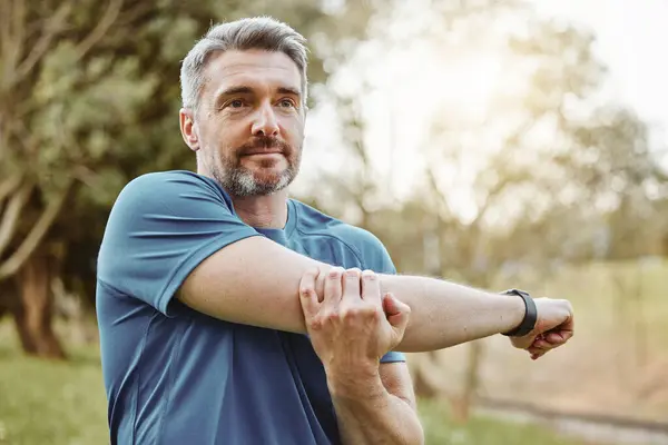 Mature man, arm stretching and outdoor for fitness, wellness and exercise in a park for health. Morning, athlete and training in nature with workout and sports of a calm person ready to start run.