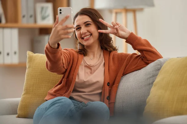 Selfie, peace hand sign and woman on couch, social media post with influencer at home and memory. Smile in picture for content creation, mobile app and relax in living room, V emoji and photography.