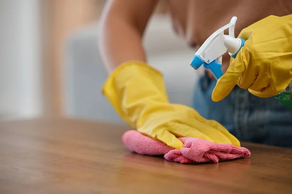 Person, hands and spray bottle in cleaning or housekeeping on table for hygiene or disinfection at home. Closeup of domestic, maid or cleaner wiping furniture or desk for bacteria or germ removal.