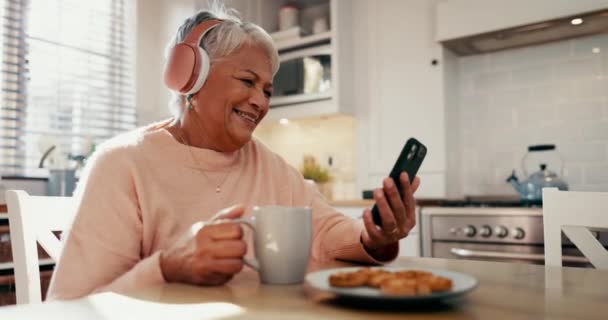 老年妇女 家里和耳机与电话 咖啡和滑稽视频通话 社交媒体或流媒体喜剧 老年人笑着 开心地听流动播客或在厨房喝茶的迷因 — 图库视频影像