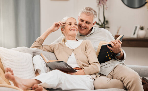 Senior, couple and reading book on a living room sofa with love, smile and retirement in a home. Elderly people, story and lounge on a couch with study for knowledge in a house happy and relax.