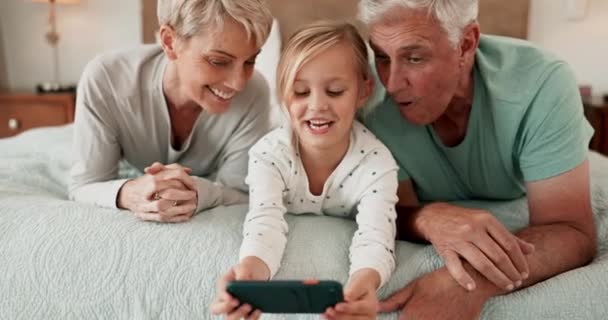还有一个女孩和她的祖父母一起在家里的床上玩 因为他们在一起玩或者在一起 孩子或与年长男人和女人及其孙女在卧室里的手机上的家庭 — 图库视频影像