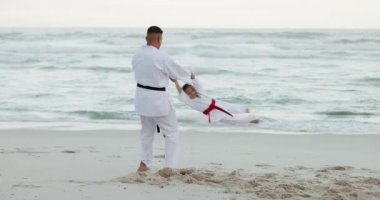 Plaj, karate ve kızını savunma çalışması için dışarı sallayan bir baba. Spor salonu, aile ya da çocuklu erkekler deniz ya da okyanus kenarında egsersiz yaparken ebeveynler ve kızlar eğleniyor..