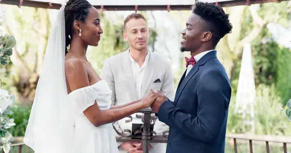 Happy black couple, wedding and vows in marriage, commitment or support together at alter. Married African woman and man holding hands for love, trust or speech of bride or groom in outdoor romance.