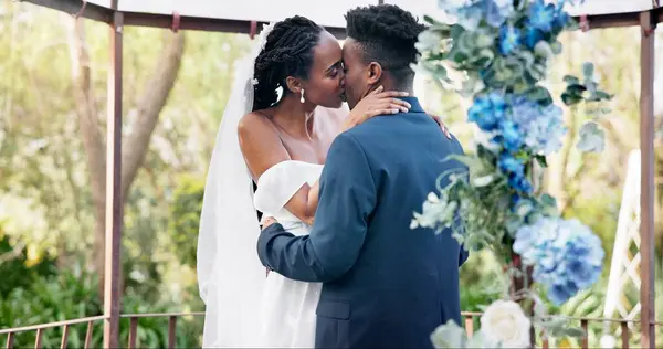 Black couple, wedding and kiss for love, marriage or commitment in embrace or hug together. Married African woman and man kissing affection, trust or relationship of bride or groom in outdoor romance.