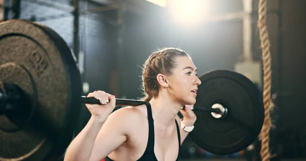 Woman at gym, weight lifting and barbell for muscle building endurance, strong body and balance power in fitness. Commitment, motivation and bodybuilder in workout challenge for health and wellness