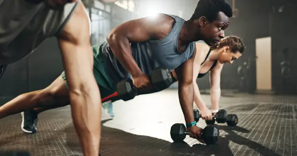 Gym group, dumbbell and rowing exercise for power, muscle challenge and action in workout class. Serious black man, strong bodybuilder and push up with heavy weights for fitness of healthy training.