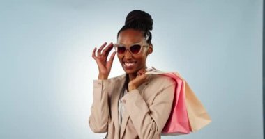 Mutlu siyah kadın, alışveriş çantası ve güneş gözlüğü moda, tarz veya satın alma, stüdyo arka planında. Afrikalı kadın portresi ya da alışverişçi gülümsemesi şık kıyafetler, indirim ya da satış için.