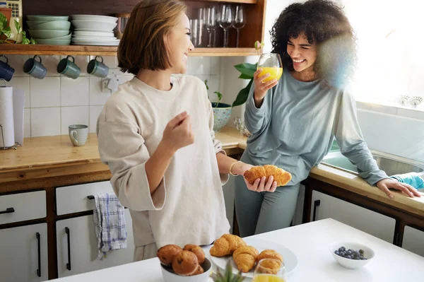 Couple, happiness and women with juice and cooking in kitchen for breakfast, nutrition and vitamin c in morning. Food, people and smile with drink and pajamas or natural face for wellness or fruit.