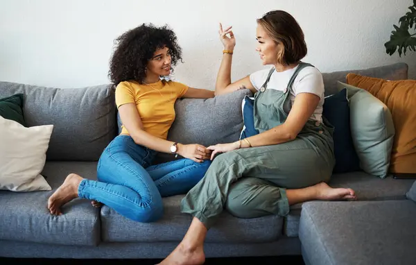 Conversation, lesbian with couple and relax on sofa in the living room talking, gossip and bonding. Happy, love and young interracial lgbtq women speaking and resting together in lounge at home.