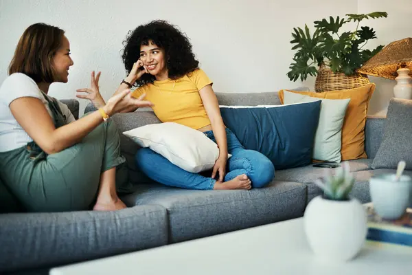 Women, friends and conversation in a home with gossip, discussion and happy in a living room. Couch, smile and people on a sofa with gossip or social together in a house lounge with speaking together.