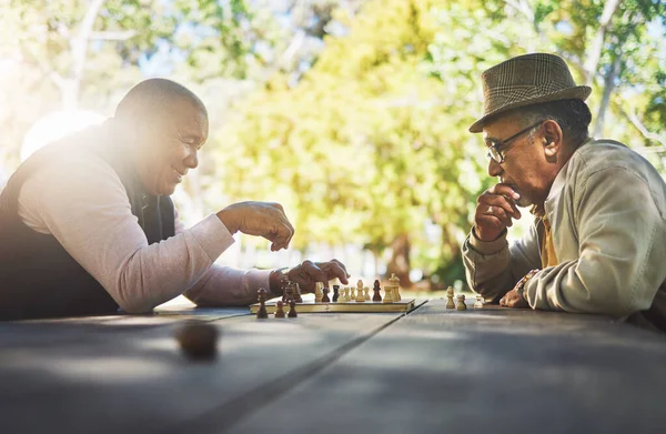 Elderly men in park, chess game and strategy with competition or challenge, friends in retirement and intelligence. Thinking, planning and contest outdoor, concentration on boardgame and recreation.