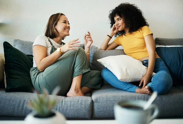 Women, friends relax and conversation in a home with gossip, discussion and happy in a living room. Couch, smile and female person on sofa with communication together in a house lounge with speaking.