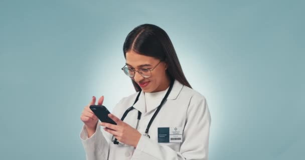 スタジオでテキストを送ったり 読んだり 青い背景で面白いミームを笑ったりするためのドクター Webチャット スクロール ソーシャルネットワークアプリでのコミュニケーションに満足している医学 看護師 スマートフォン — ストック動画