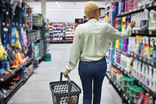 Back, shopping in a grocery store and a woman customer looking to purchase a product for retail spending. Supermarket, shelf or choice of food with a consumer or shopper carrying a basket in an aisle.