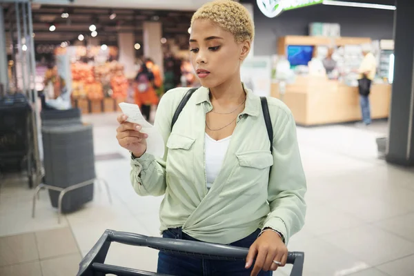 Woman, grocery shopping and receipt for budget, inflation or price check in supermarket of sale or discount. African customer with cost of living, retail and food choice or paper at convenience store.