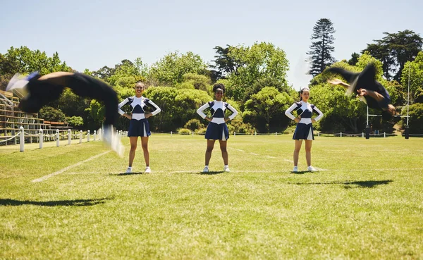 Cheerleader team, practise or sports field for exercise, routine and uniform for fitness, dancers or support. Students, motion or in air for dance, wellness and train with smile, energy and formation.