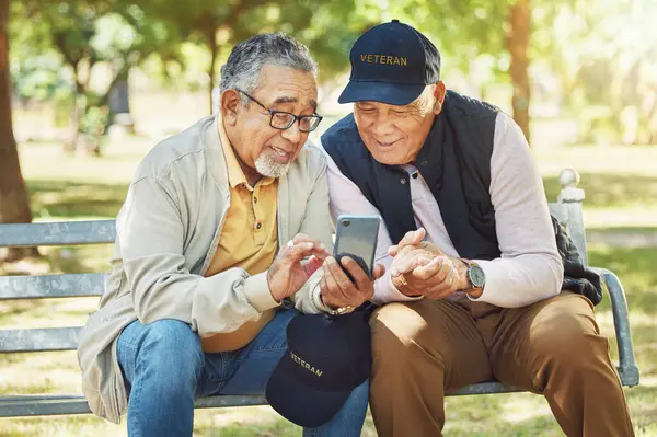 Elderly men, friends and phone in park, reading and army memory with thinking, relax and sunshine. Senior military veteran, smartphone social media and talk on bench, nostalgia and remember service.
