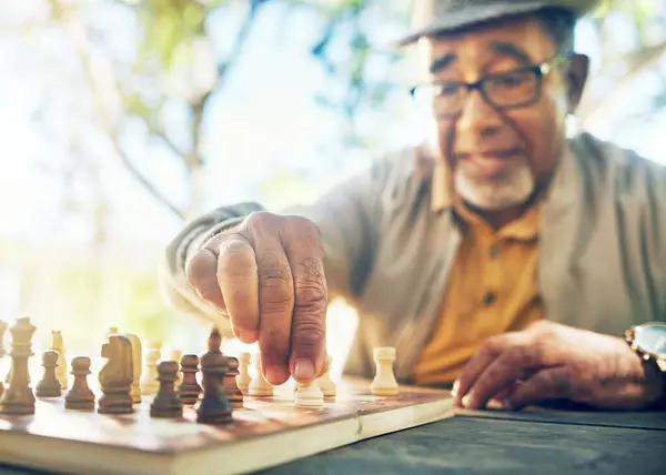 Old man in park, hand with chess game and strategy, competition or challenge, retirement and moving piece. Closeup, planning and contest outdoor, concentration on boardgame and recreation in nature.