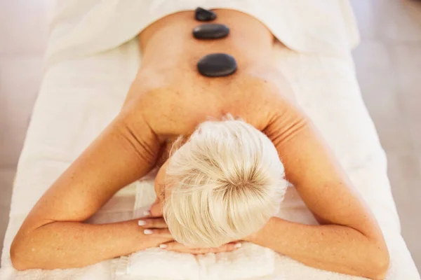 Senior woman, spa and wellness with stone, massage and relax with health, stress relief and luxury. Salon treatment, elderly person and pensioner with care, resting and spine with beauty and rock.