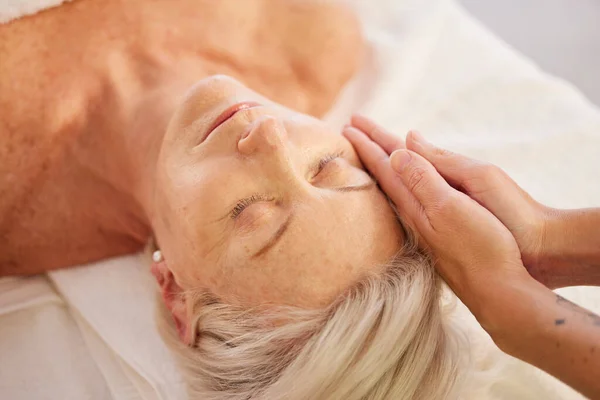 Relax, face massage and senior woman at a spa for luxury, self care and facial healing treatment. Health, wellness and elderly female person on a retirement retreat for head therapy at natural salon