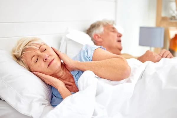 Snoring, problem and woman with frustrated with noise, sound or husband sleeping in bed with wife. Elderly, couple and man snore in sleep in retirement home bedroom and lady with hands on ears.