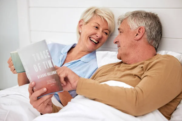 Bed, book and senior couple with love, conversation and marriage with creativity, relax and retirement. Novel, storytelling and old woman with elderly man, bedroom and home with discussion or resting.