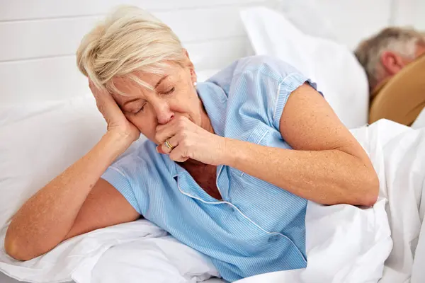 Couple, coughing or sick old woman in bed with husband or man with flu virus, tuberculosis or health problem. Chest pain, mature lady or senior person with cold, fever or lung illness in home bedroom.