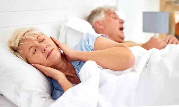 Snoring, problem and woman with frustrated with noise, sound or husband sleeping in bed with wife. Elderly, couple and man snore in sleep in retirement home bedroom and lady with hands on ears.