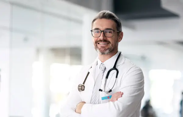Happy doctor, portrait and man with arms crossed in hospital for healthcare, wellness or career. Face, medical professional smile and confident surgeon, expert or mature employee in glasses in Canada.