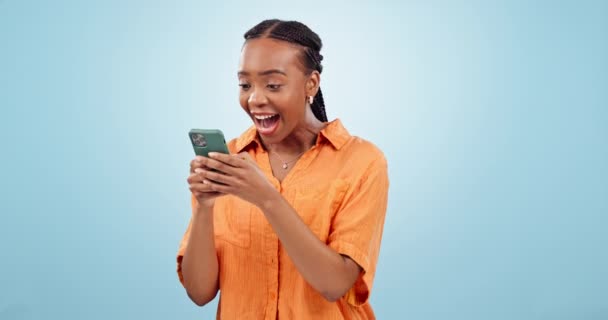 スマートフォン 黒人女性に興奮し スタジオ お祝い ソーシャルメディアで青い背景に魅了されます オンラインコンペで幸せ 報酬のためのダンス — ストック動画