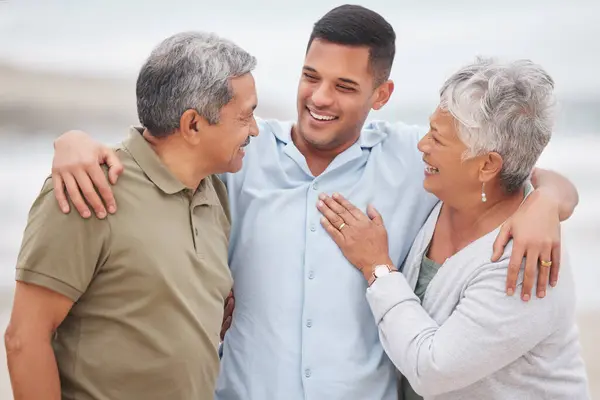 Man, senior parents or laughing at beach for bond, support or love with smile, care or pride in retirement. Hug, father or mature mother with a happy son at sea together on family holiday vacation.