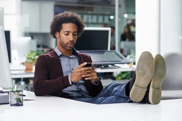 Its good to be the boss. Shot of a young businessman sending a text message with his feet on a desk