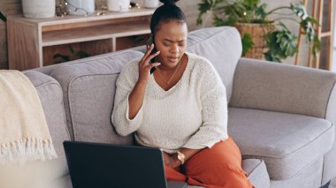 Laptop, telefon görüşmesi ve sorun çözmek için evinin oturma odasındaki kanepede oturan siyahi bir kadınla endişelen. Bilgisayar, iletişim ve cep telefonunda ağ kurmak için konuşan ilgili bir kişi..