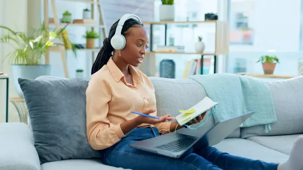 African woman, student and laptop for online course on sofa, headphones and notes with thinking in home. Girl, reading and ideas with notebook, computer or headphones for study on video call on couch.