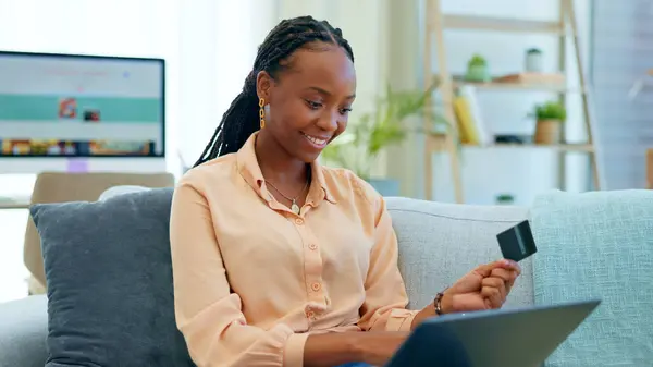 Happy black woman, laptop and credit card on sofa for payment, online shopping or banking at home. African female person smile with debit and computer for finance, fintech or ecommerce in living room.