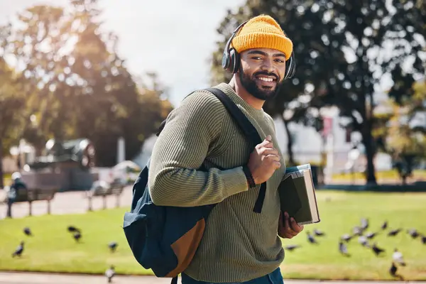 Student, headphones and backpack for outdoor education, college or university podcast in park or campus. Portrait of african man walking, travel and books with study, learning and listening to music.