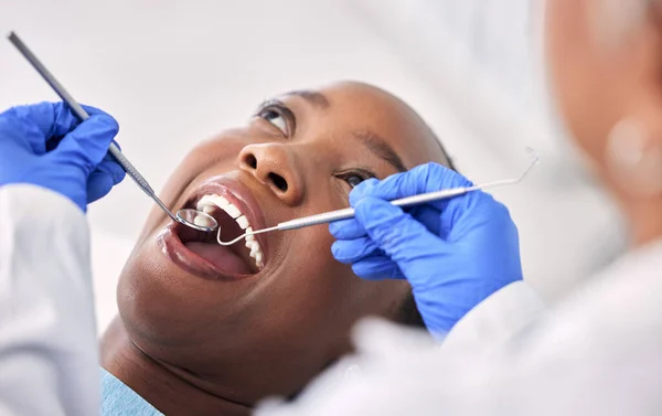 Dentist, patient and women at clinic, tools in consultation and check mouth for dental health and medical treatment. Oral hygiene, healthcare and surgery, orthodontics and tooth decay with excavator.
