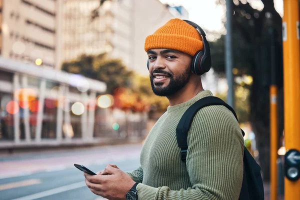 Phone, headphones and portrait of man in city outdoor, listen to audio or radio sound on internet to travel. Face, streaming music and happy student typing in street on social media in South Africa.