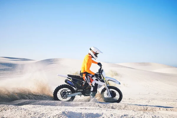 Extreme sport, motorcycle and athlete with sand by wheels with pride, skill and adrenaline rush. Biker, sunshine and dust with blue sky in fun, fitness and achievement in speed, race and lens flare.