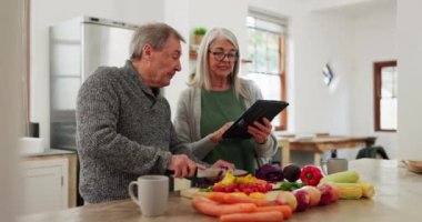 Mutfakta yaşlı bir çift, tabletle yemek pişiriyor ve sebze beslenme fikrine online tarifte yardımcı oluyor. Sağlıklı yemek, kıdemli erkek ve kadın yemek hazırlama, diyet ve öğle yemeği için dijital uygulaması olan evde..