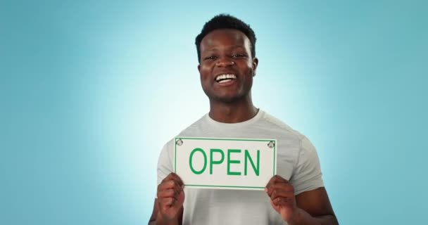 ハッピーブラックマン オープンサイン 広告を歓迎または青い背景に対するサービスの準備ができています アフリカの男性の人物の肖像画または店の所有者の笑顔はモックアップでマーケティングのための掲示板を示します — ストック動画