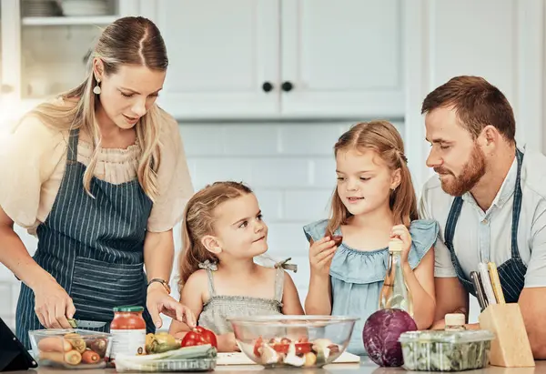 Happy family in kitchen, cooking together with children and teaching, learning and nutrition with parents. Mom, dad and girl kids help making healthy food in home with care, support and love at lunch.