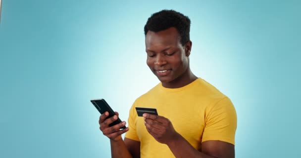 オンラインショッピング フィンテックの支払い 青色の背景でのプロモーションのためのスマートフォンで興奮した 男とクレジットカード アフリカのモデル モバイルバンキングアプリ Eコマースの成功 スタジオでの取引または販売 — ストック動画