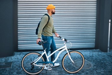 Şehir, yürüyüş ve sabah üniversiteye çevre dostu ulaşım için sokakta bisikletli bir adam. Şehir kaldırımı, karbon nötr yol ve bisiklet, sırt çantası ve sabah seyahati ile üniversite öğrencisi