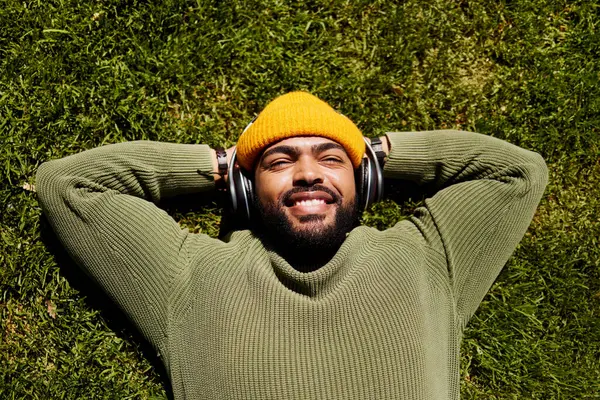 Relax, music headphones and happy man on grass outdoor, listen to audio online or hearing sound of podcast from top view. Smile, streaming radio and person at park resting for peace, calm and freedom.
