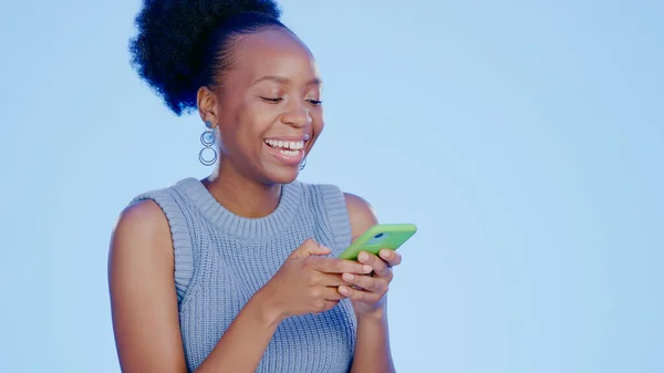 stock image Cellphone, happy and black woman in a studio networking on social media, mobile app or the internet. Smile, technology and young African female model scroll on a phone isolated by blue background