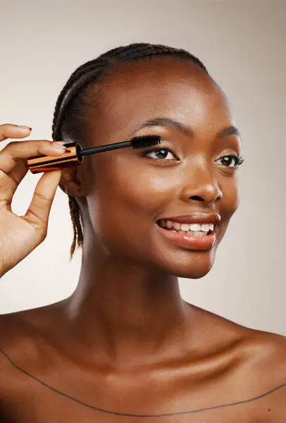 Mascara, happy woman and makeup in studio for beauty, cosmetics and smile on brown background. African model, makeover and brush lashes for skincare application, aesthetic tools and eyelash extension.