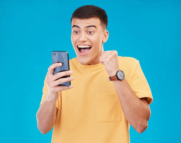 携帯電話 お祝い そして勝利 成功または達成のための拳ポンプを持つスタジオの若者 カナダのハッピー 男性優勝者 青色の背景で隔離された電話で賞品を応援 — ストック写真