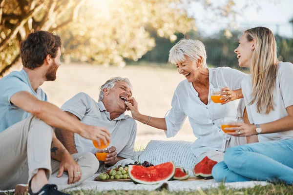Picnic, laughing family and senior parents, daughter and son having fun, eating grapes and enjoy outdoor nature, park or bond. Watermelon fruits, comedy and relax elderly mom, dad or people together.